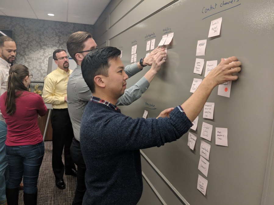 Five 10 up team members in a work session hanging pink post-its against a wall