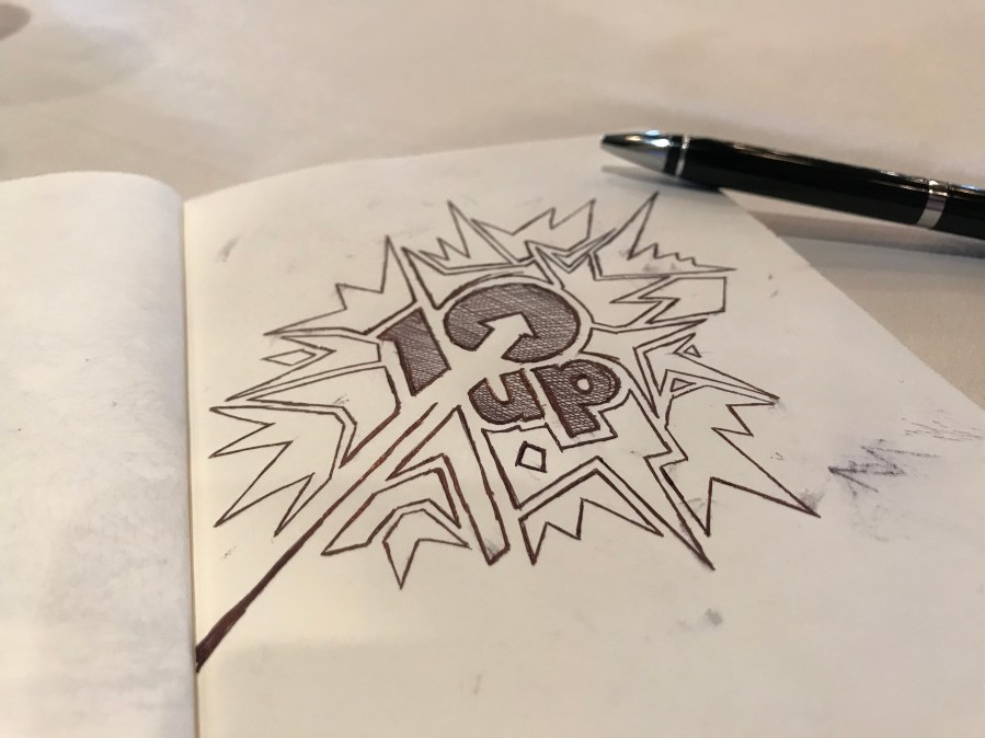 Notebook splayed open showing a doodle of the 10up logo and a pen alongside