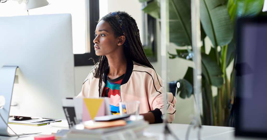 A person sitting at a desk and working on a laptop with other office supplies scattered on the table