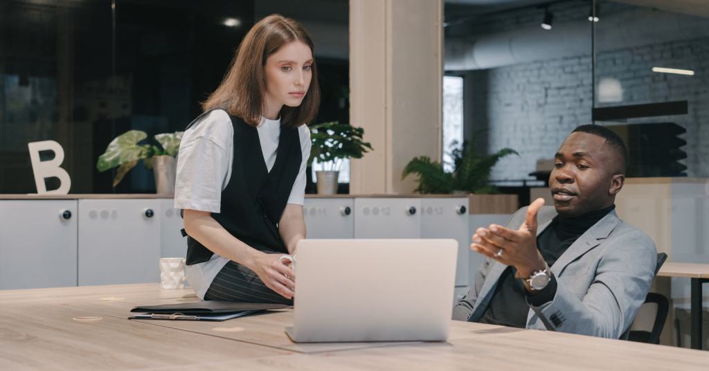 A person sitting at a table who is showing something on a laptop to another person who is sitting on the table