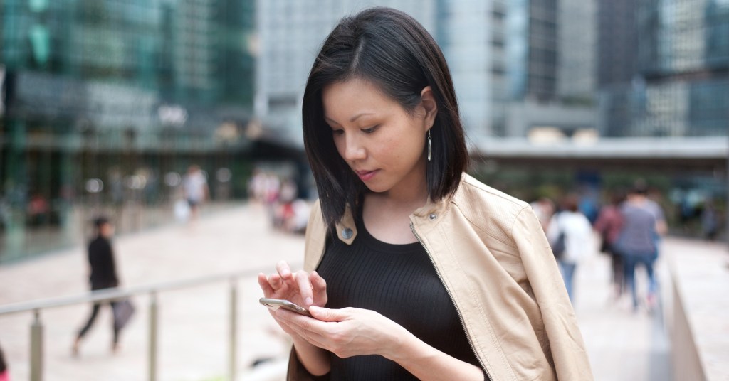 A person looking down at their phone while standing outside in a public area