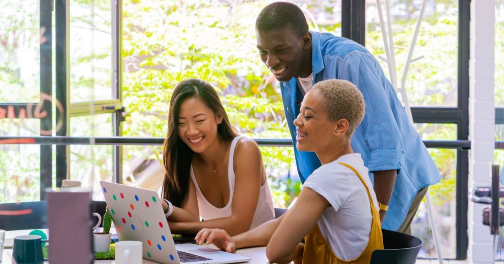 Three people smiling while looking at the screen of a polka dot laptop