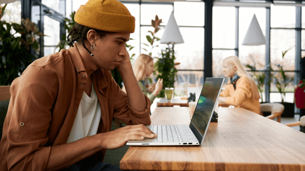 A person sitting at a wooden table while looking at a laptop