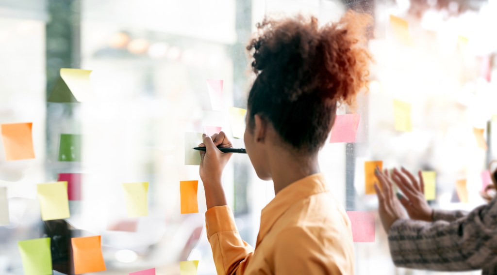 Young businesswoman creative team using post it notes in glass wall to writing strategy business plan to development grow to success.