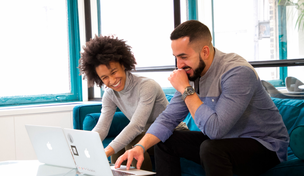 Two people looking at laptops and laughing